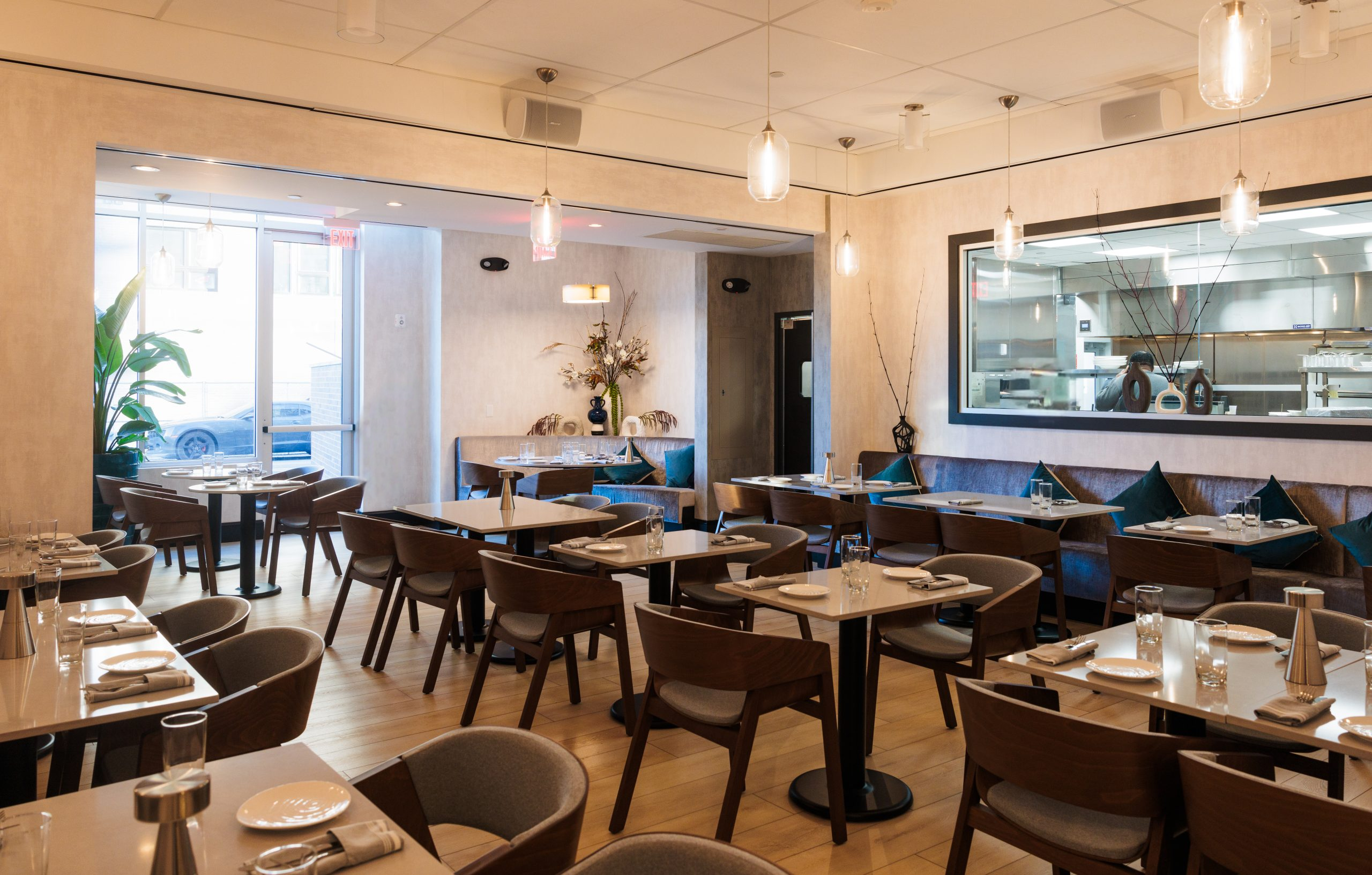 The elegant dining area at OU LA restaurant, featuring a modern and sophisticated design with warm lighting, wooden furnishings, and plush seating. The open kitchen window adds a dynamic touch, allowing guests to glimpse the culinary artistry behind the Caribbean-inspired fine dining experience.